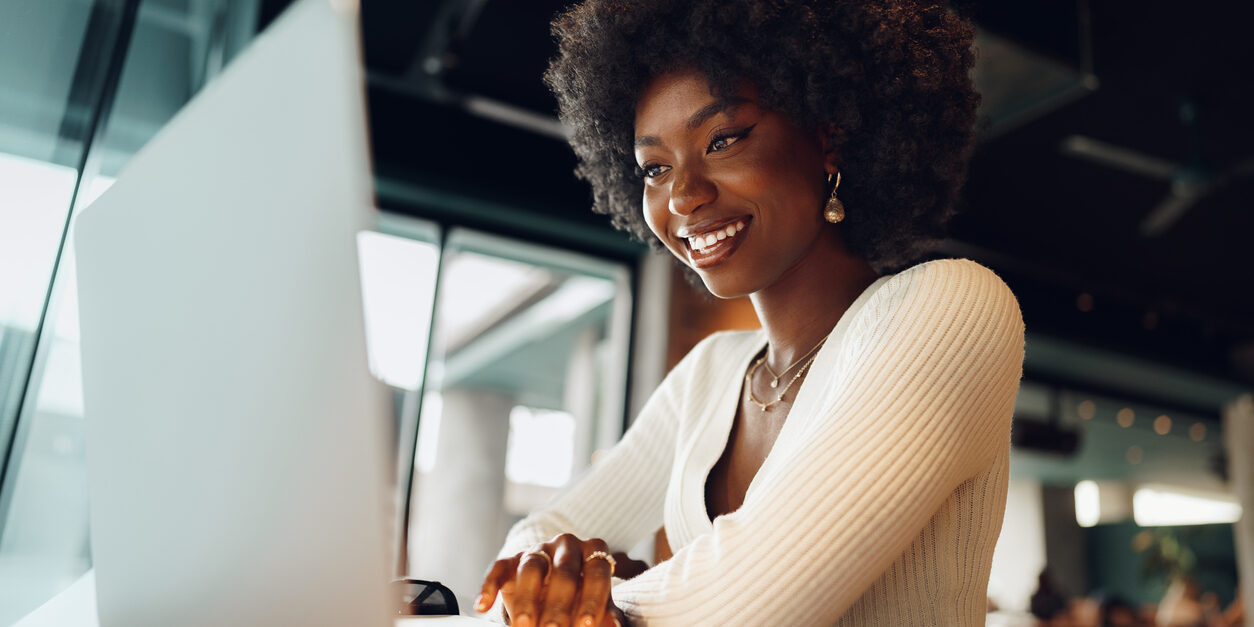 Smiling young african woman sitting with laptop in cafe, portrait